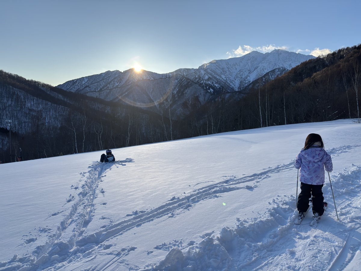 鹿島槍スキー場のゲレンデ。夕日が山の稜線に沈むなか、子どもがスキーで斜面を登っている